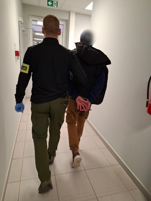 policjant podczas doprowadzenia zatrzymanego