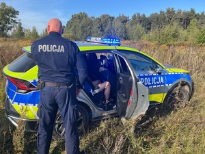 policjant i radiowóz policyjny z pasażerem auta, którego kierujący nie zatrzymał się do kontroli